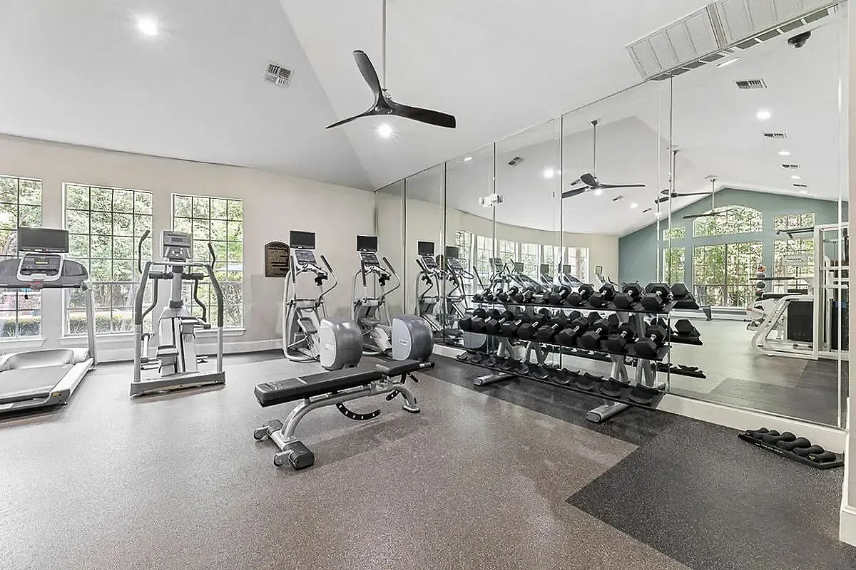 Modern fitness center equipped with state-of-the-art cardio machines, free weights, and mirrored walls for an invigorating workout experience at Raveneaux Apartments in North Houston