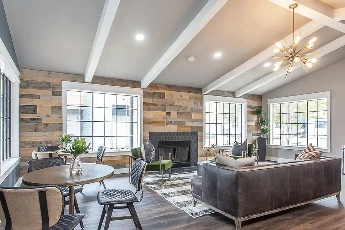 Modern clubroom at Steepleway Downs Apartments with stylish wood-paneled walls, cozy fireplace, elegant chandelier, and large windows for natural light.