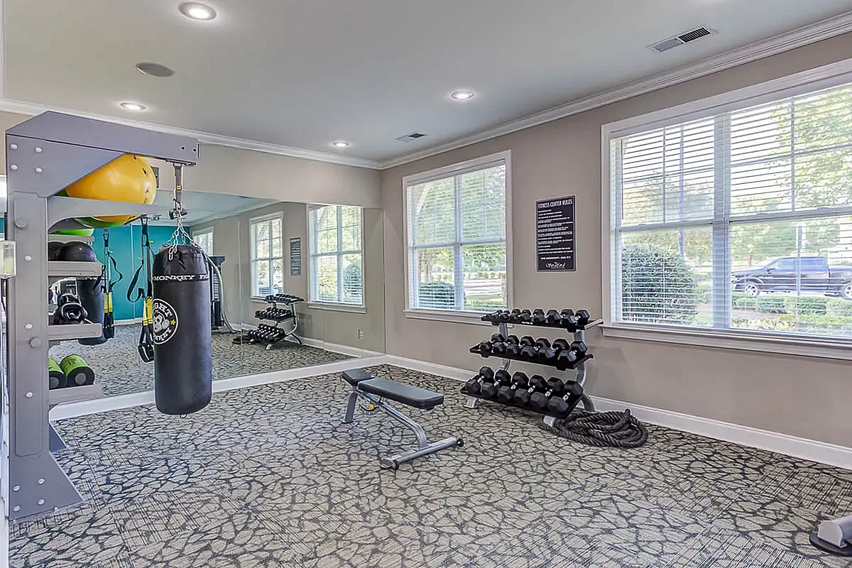 Inviting fitness center at The Stratford at Hillcrest Towne Center Apartments with modern equipment, including weights, a bench, and a punching bag, illuminated by ample natural light through large windows.