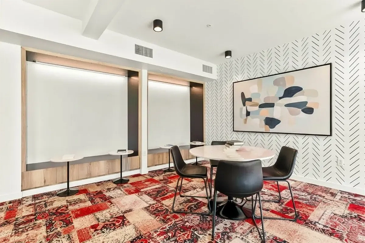 Stylish dining area with a round table, modern chairs, patterned carpet, and contemporary art on the wall at 805 Riverfront Apartments in Sacramento