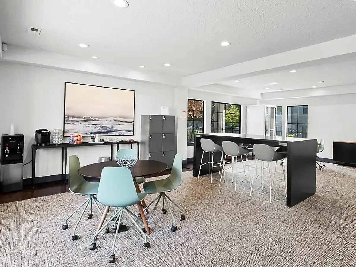 Modern communal lounge with sleek bar seating, a cozy round table, and vibrant artwork, ideal for socializing or relaxing  at Apt CoWork at Cottonwood Apartments in Salt Lake City