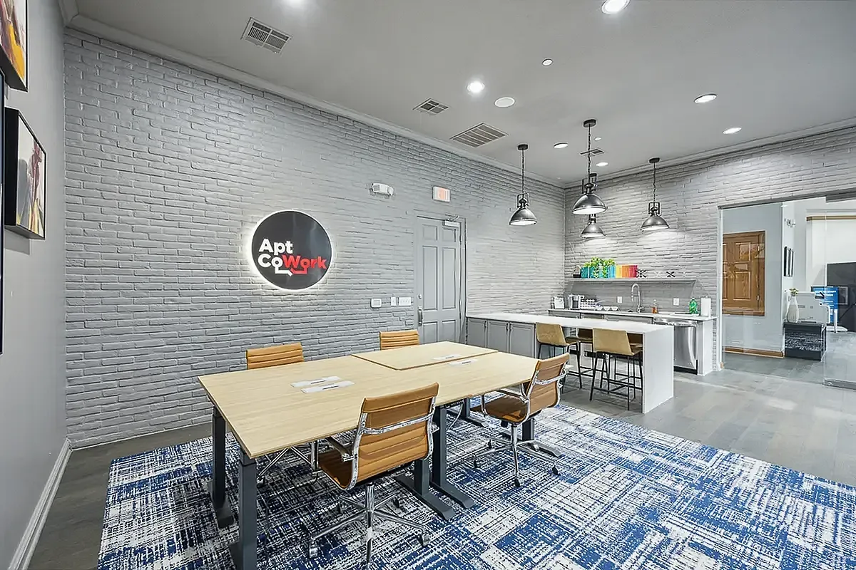 Modern co-working space at Cottonwood Ridgeview Apartments with sleek design, featuring a conference table, comfortable chairs, a kitchen area, and contemporary lighting in a stylish office setting.