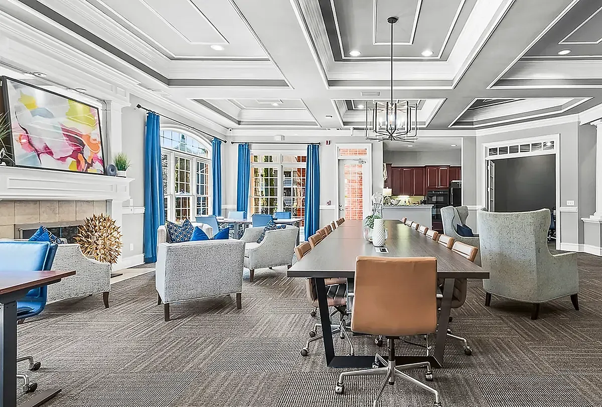 Elegant and spacious workspace at Retreat at Peachtree City Apartments with stylish furniture, modern chandelier, and vibrant blue accents, perfect for gatherings.