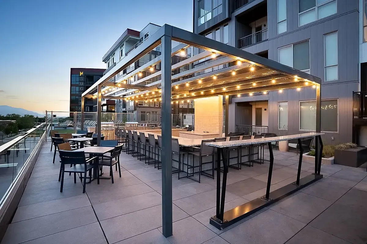 Elegant rooftop patio at Sugarmont in Salt Lake City, UT with modern pergola, sparkling string lights, and ample seating, offering stunning sunset views for social gatherings.