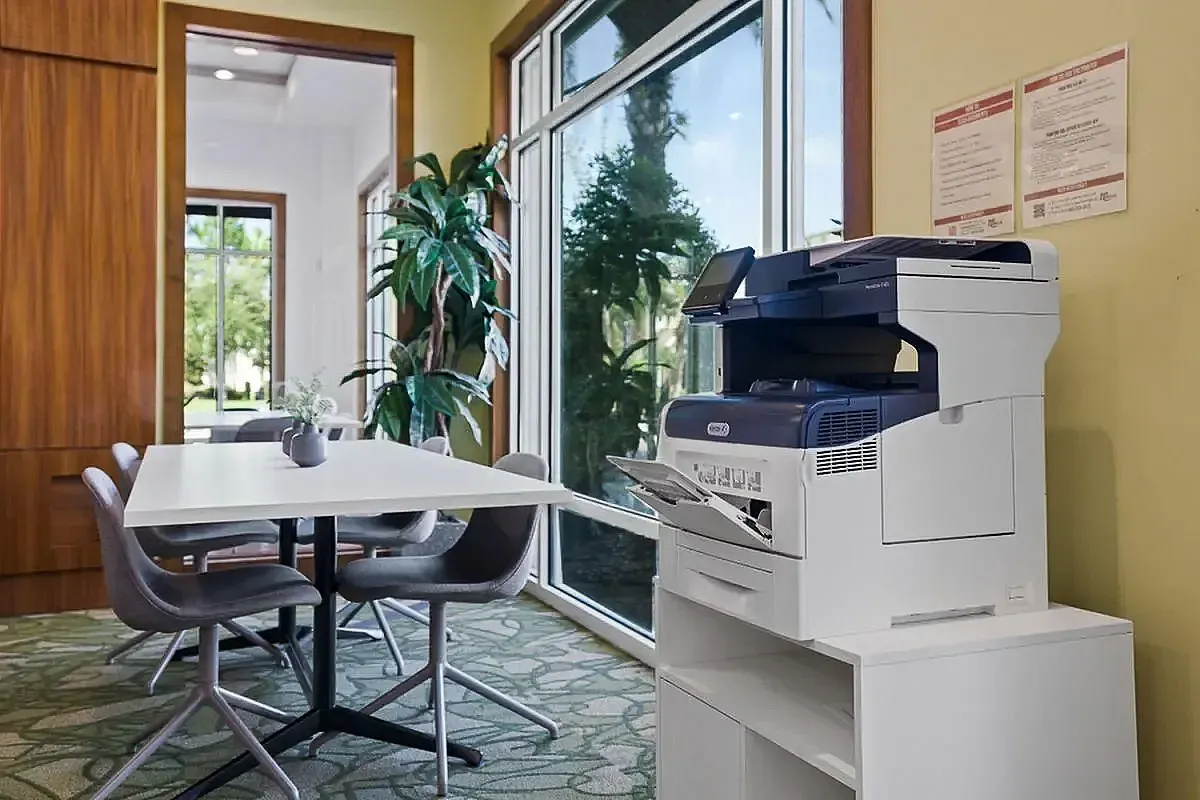 Bright and modern business center with a spacious meeting table, sleek gray chairs, and a high-tech multifunction free printer at the Marq Highland Park Apt CoWork in Westchase Tampa