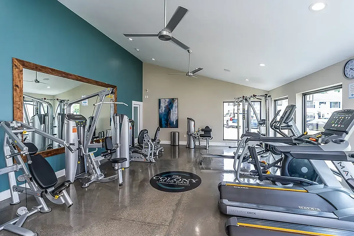 Bright and modern fitness center at The Colony at the Oaks Apartments featuring state-of-the-art equipment and large mirrors, perfect for an energizing workout experience.