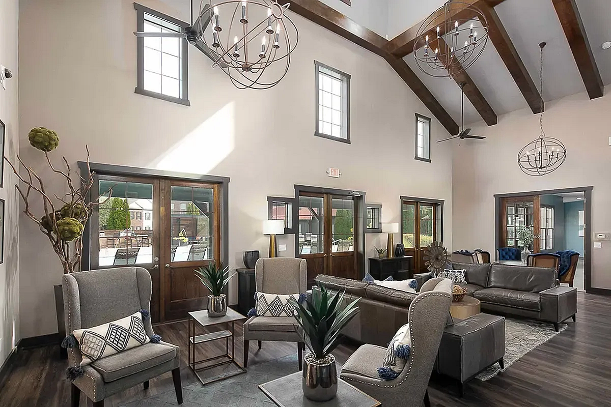 Luxurious clubroom at The Mill at Georgetown Apartments with high ceilings, large windows, elegant chandeliers, and plush seating in a contemporary design.