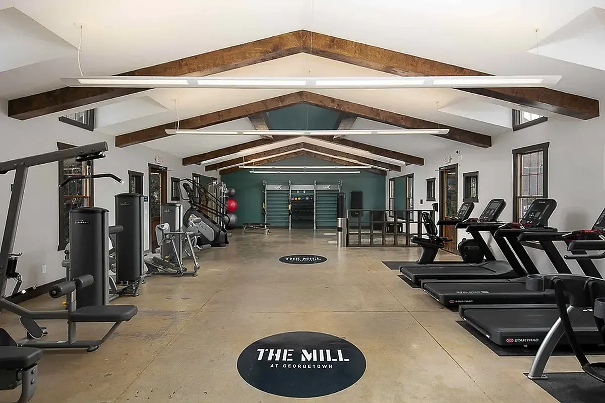 Modern gym at The Mill at Georgetown featuring state-of-the-art fitness equipment, treadmills, and a dynamic training area with stylish wooden beam ceiling.