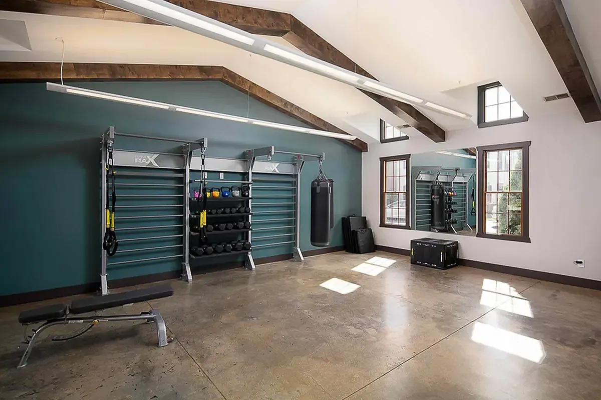 Contemporary gym at The Mill at Georgetown Apartments with high ceilings, equipped with professional training equipment, punching bag, and natural light streaming through large windows.