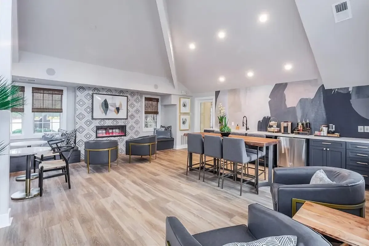 Chic open-concept clubhouse at The Retreat at Stillmeadow Apartments with stylish decor, featuring a modern fireplace, elegant wooden flooring, and a sleek kitchen island with bar stools.