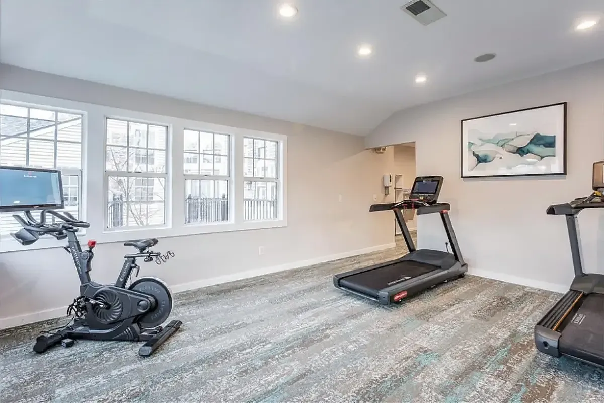 Bright and modern fitness room at The Retreat at Stillmeadow Apartments featuring state-of-the-art exercise bike, two sleek treadmills, and a wall-mounted TV.
