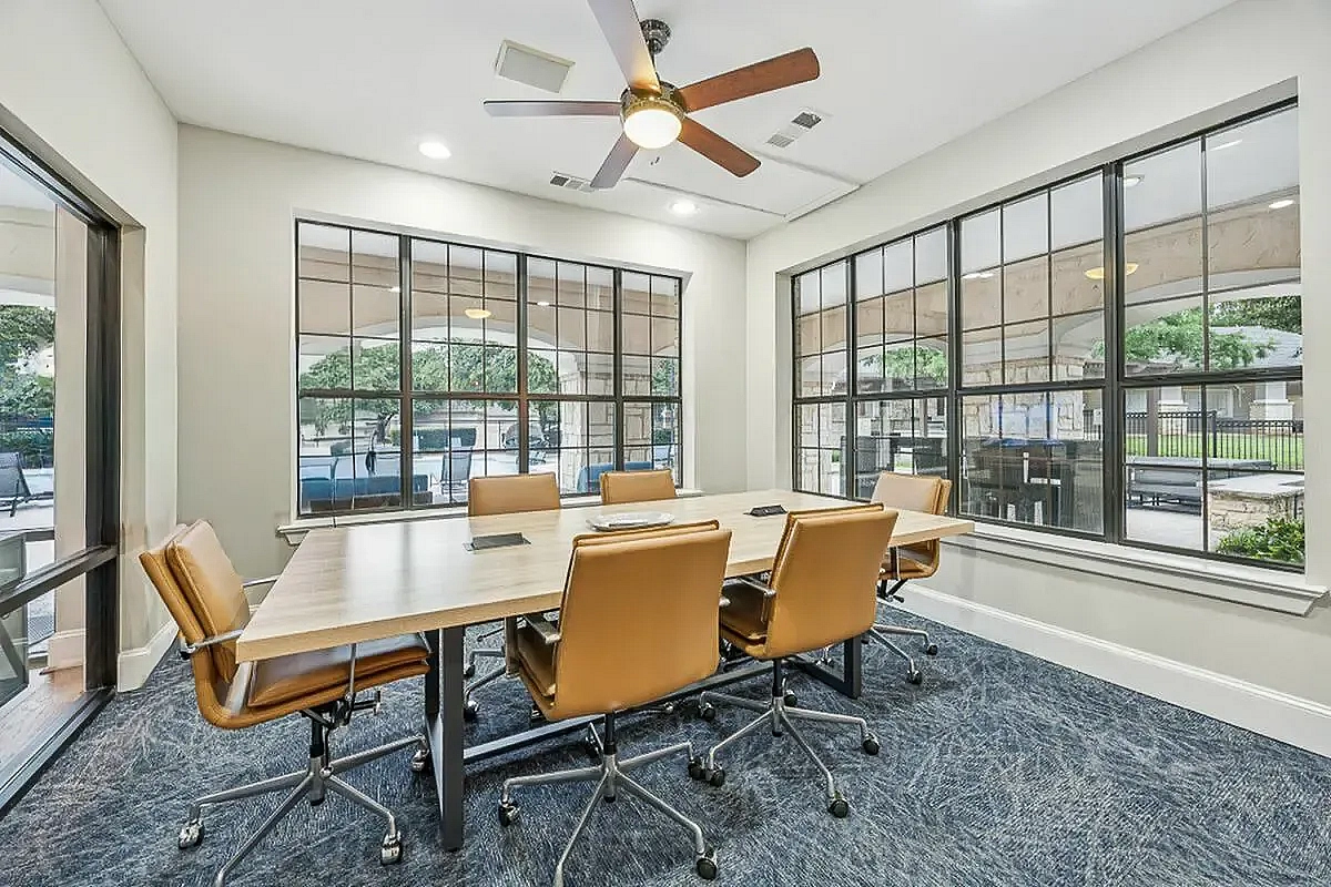 Inviting conference room with modern furnishings, large windows offering natural light, and a wall-mounted screen for presentations at Apt CoWork at Toscana at Valley Ridge Apartments in Lewisville Texas