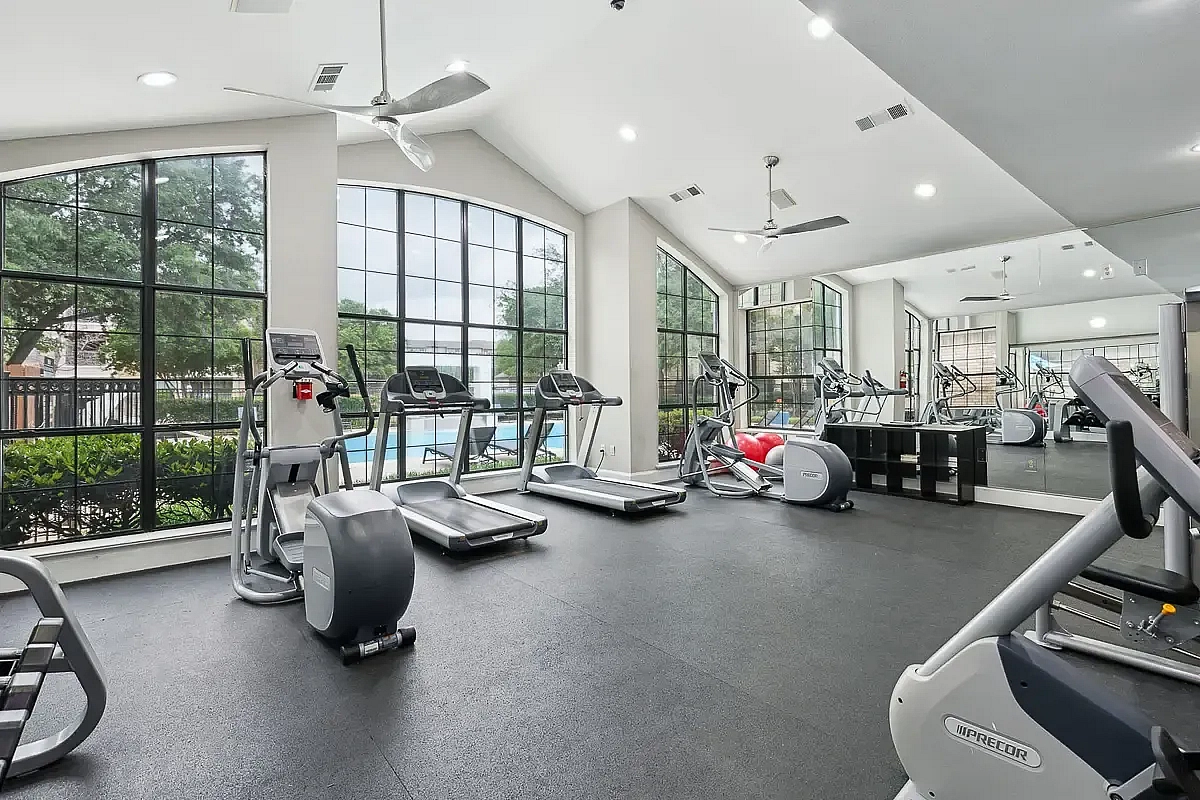 Spacious gym with large windows, featuring treadmills and elliptical machines, offering a vibrant workout environment with a pool view at Toscana at Valley Ridge.