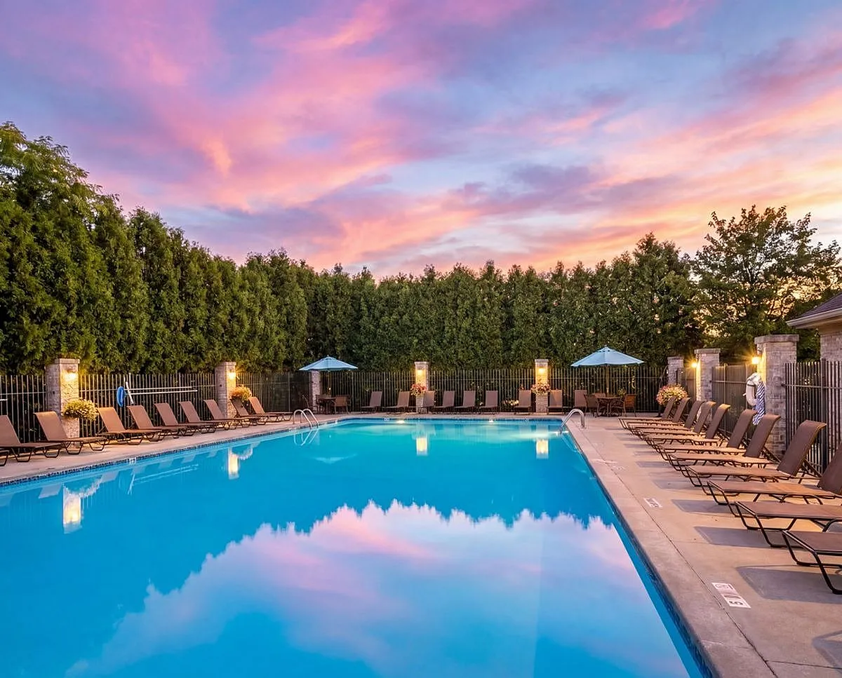Luxurious outdoor pool area with inviting lounge chairs and umbrellas, set against a stunning sunset sky and lush greenery at Clearview Apartments in Holland, MI