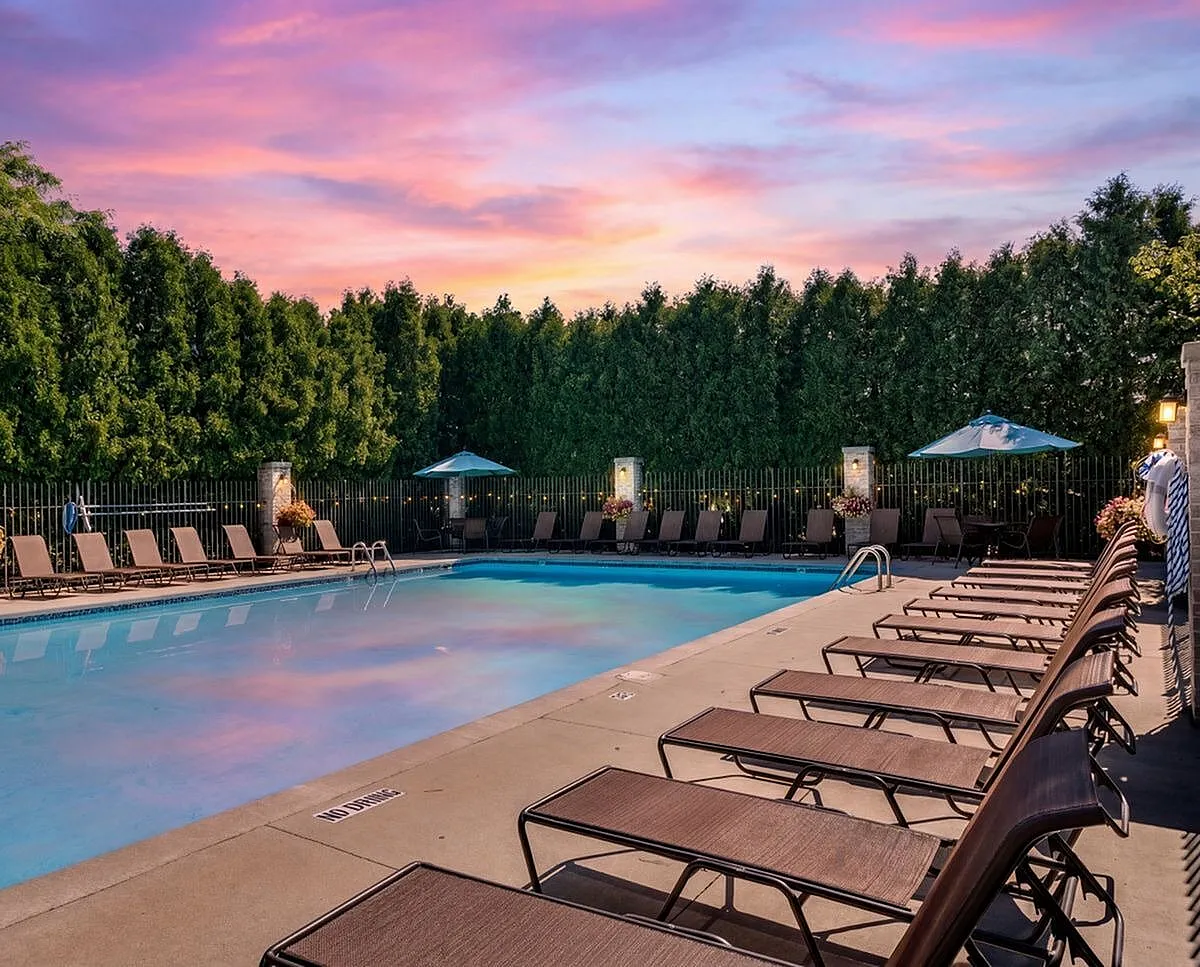 Inviting outdoor pool area with elegant lounge chairs at sunset, surrounded by lush greenery Clearview Apartments in Holland, MI