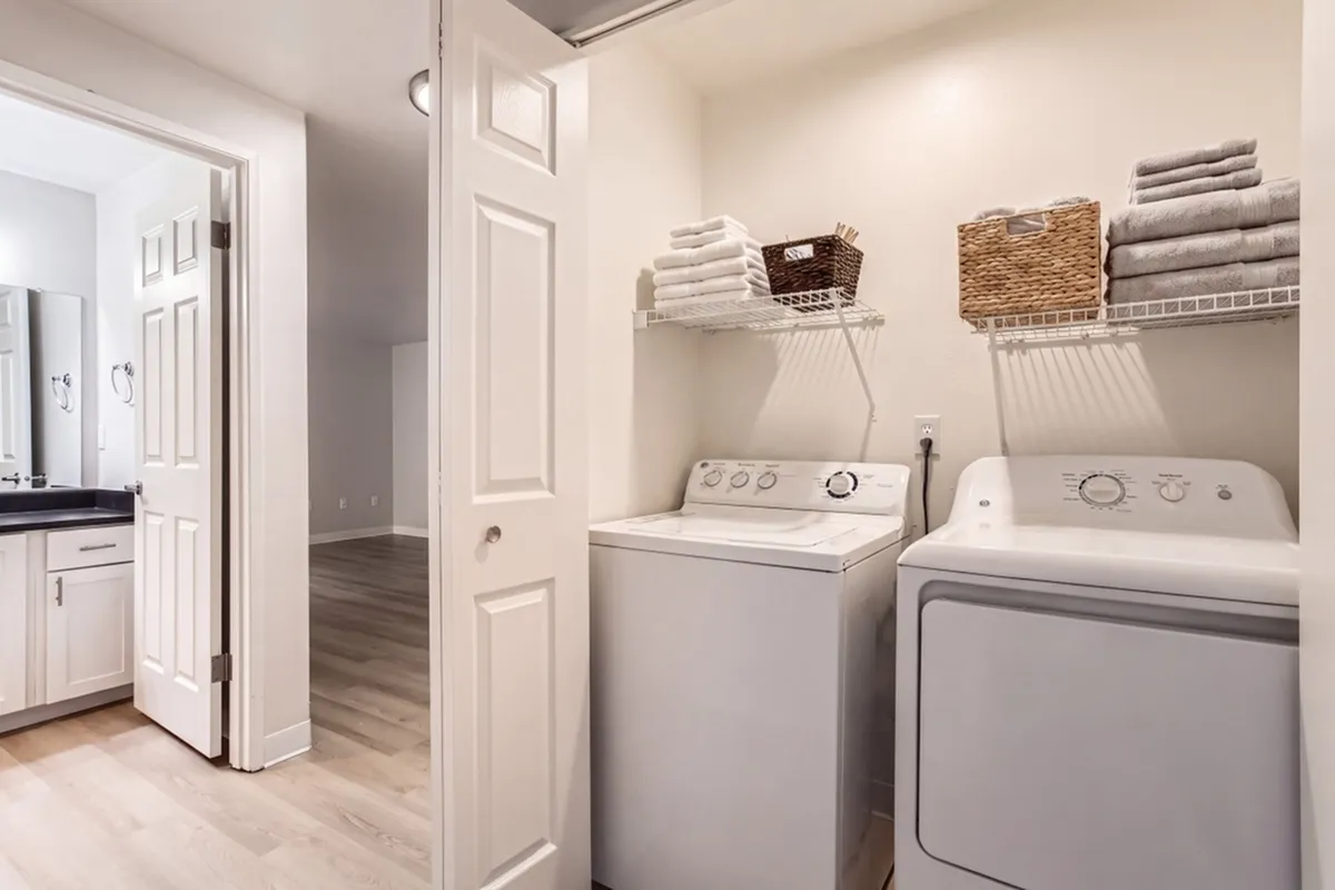 Modern apartment laundry area with washer, dryer, and ample shelving for storage in a bright, spacious setting.