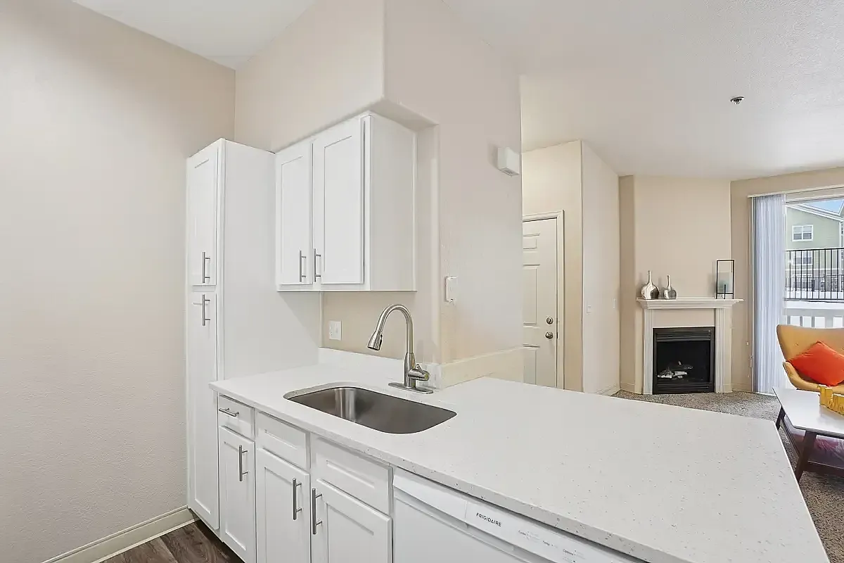 Modern apartment interior showcasing a sleek kitchen with white cabinetry, and a cozy living area with a stylish fireplace and natural light.