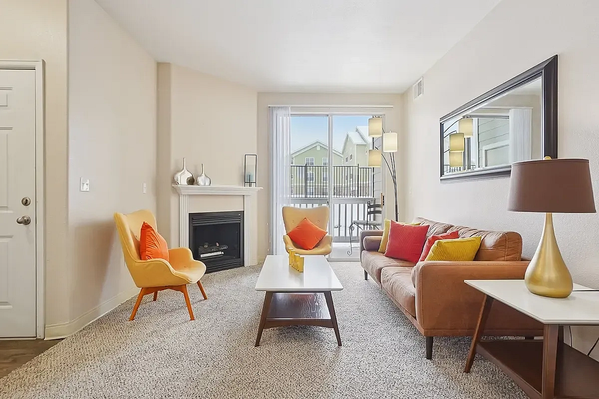 Bright and inviting living room with modern decor, featuring a cozy fireplace, stylish furniture, and vibrant cushions, with natural light streaming through sliding glass doors.