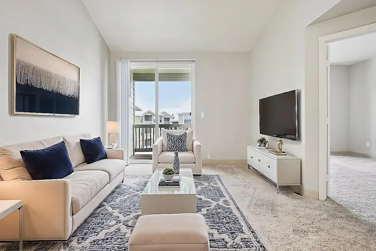 Bright and contemporary living room featuring elegant furnishings, a stylish TV setup, and access to a private balcony with scenic views.