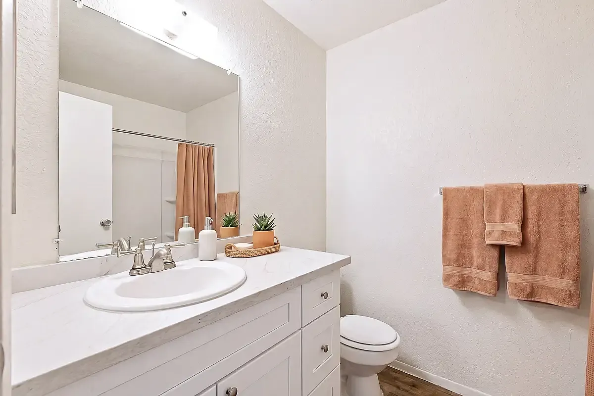 Bright and inviting bathroom at Camelot Apartments in Yuma with a sleek white vanity, large mirror, and elegant decor. Featuring plush towels and modern fixtures for a luxurious touch.