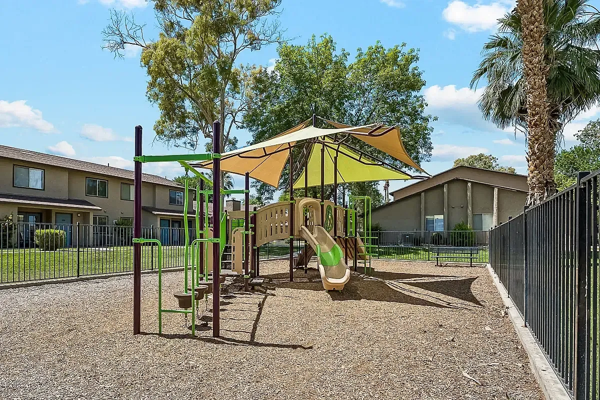 Charming community playground with vibrant playscape and shaded seating, perfect for family fun and relaxation at Camelot Apartments in Yuma.