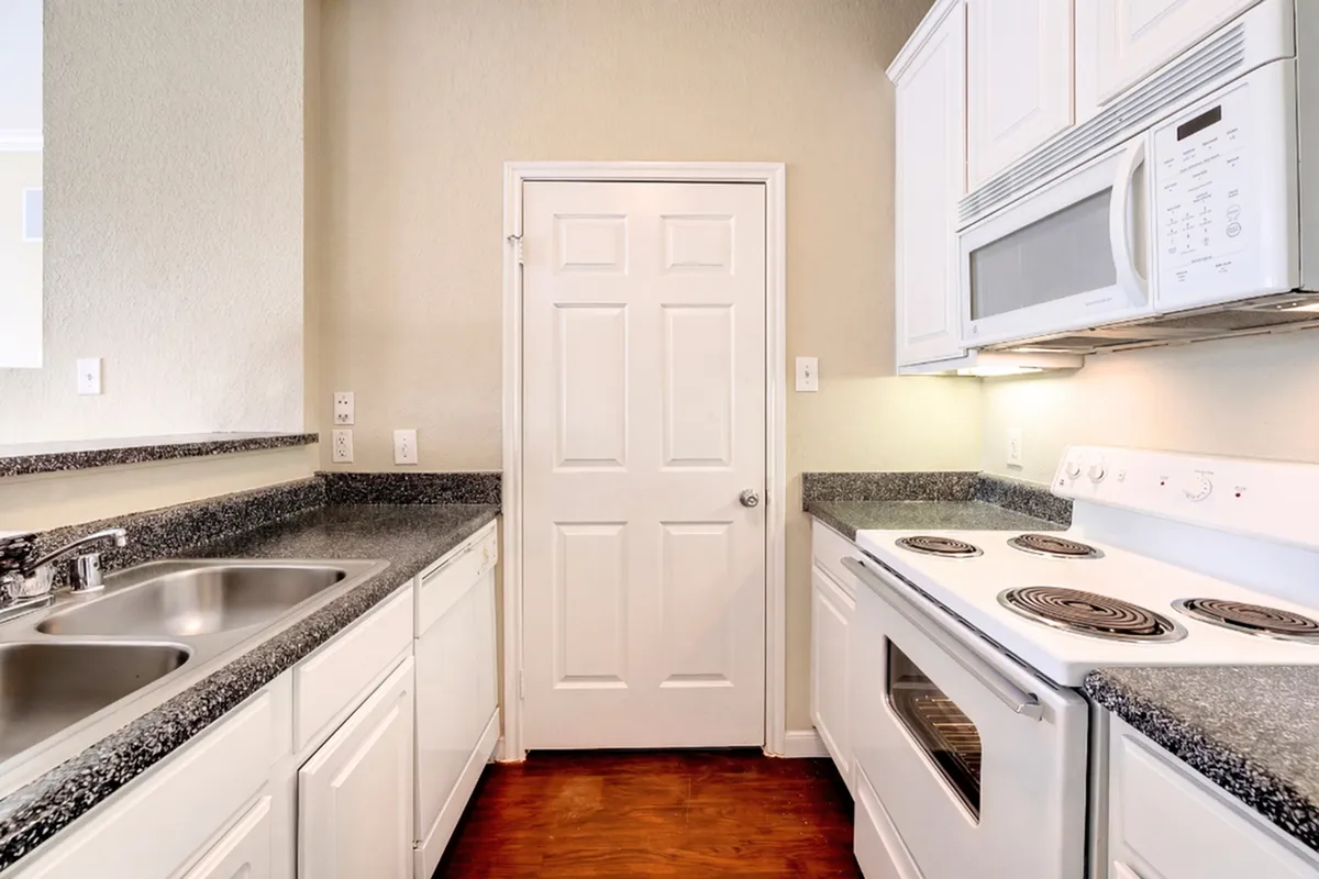 Modern kitchen with sleek granite countertops and white cabinetry, featuring a built-in microwave and electric stove for seamless culinary experiences.