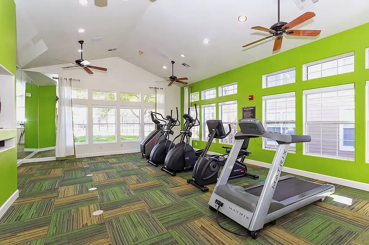 Bright and modern fitness center with state-of-the-art treadmills and ellipticals, featuring vibrant green accents and ample natural light The Orchards at Cherry Creek Park Apartments.