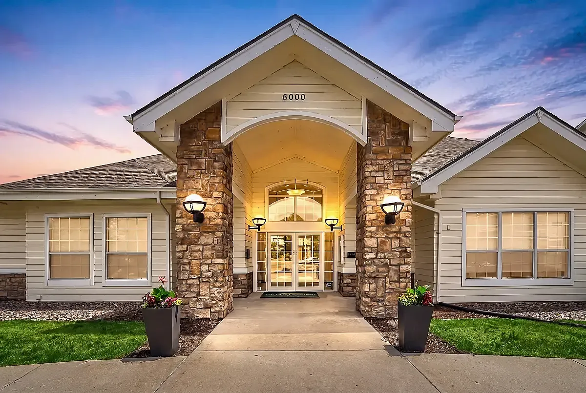 Charming modern apartment leasing office with elegant stone pillars and warm ambient lighting under a twilight sky at The Orchards at Cherry Creek Park Apartments in Centennial.