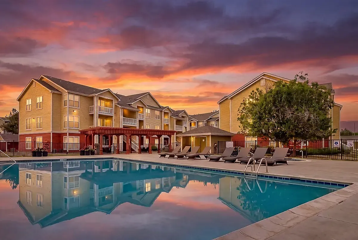 Charming sunset view of a lovely apartment complex, The Orchards at Cherry Creek Park, featuring serene poolside relaxation and elegant lounging chairs.