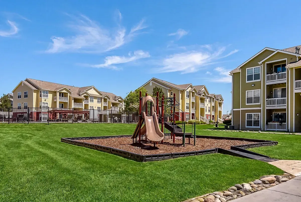 Inviting apartment community in Centennial with charming playground and lush green lawns under a bright blue sky, ideal for family living.