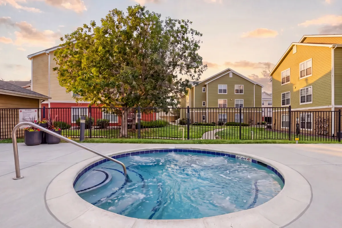 Inviting residential courtyard featuring a bubbling hot tub, lush landscaping, and vibrant multi-story houses under a picturesque sunset.