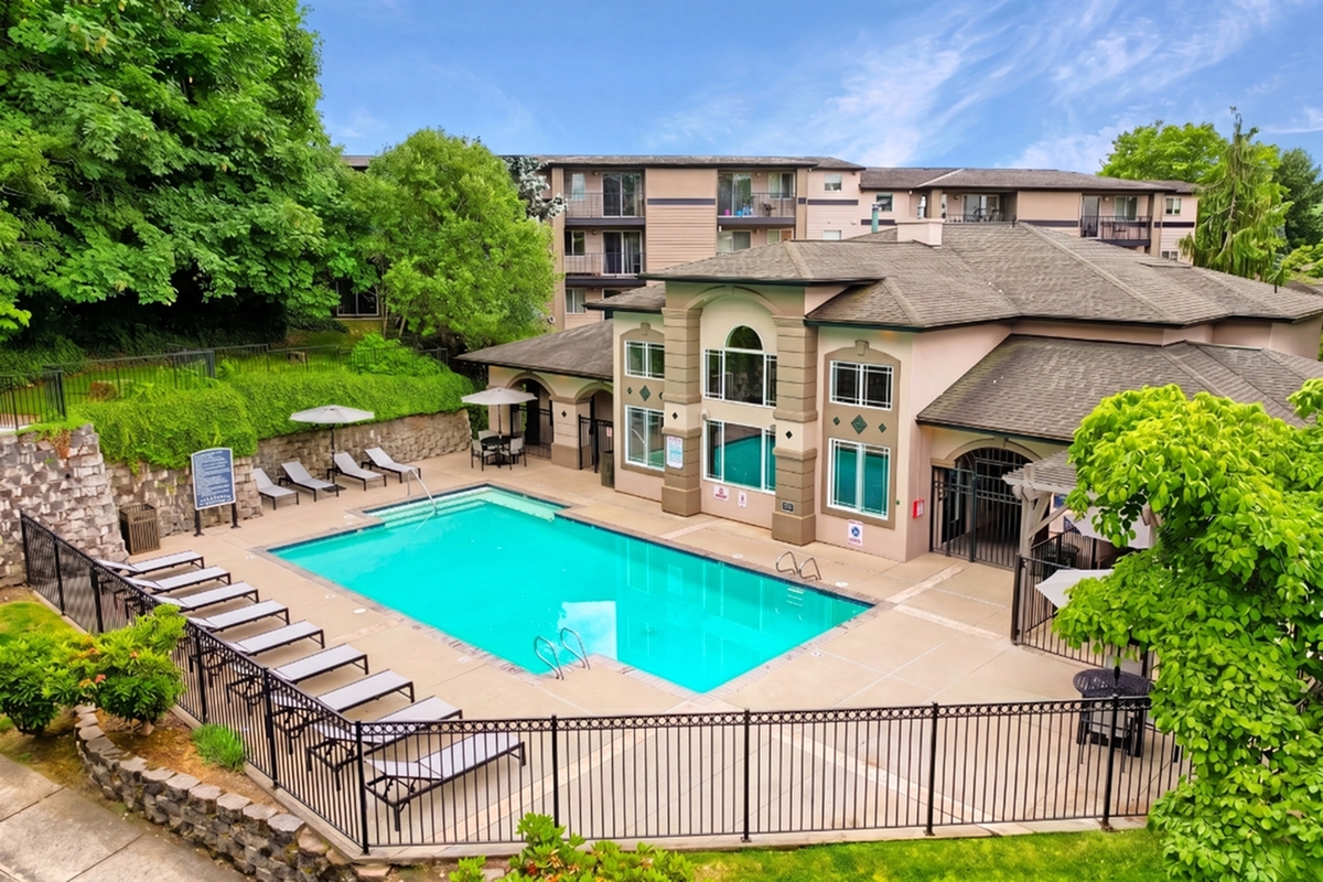 Elegant apartment complex featuring a beautiful outdoor swimming pool, surrounded by lush greenery and comfortable lounge chairs.
