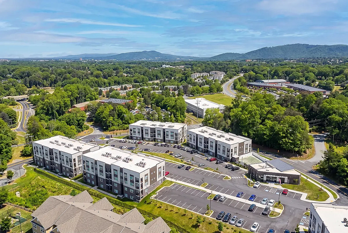 Aerial view of modern apartment complex surrounded by lush greenery and rolling hills, featuring multiple buildings and spacious parking at 5 Row Apartments in Charlottesville.