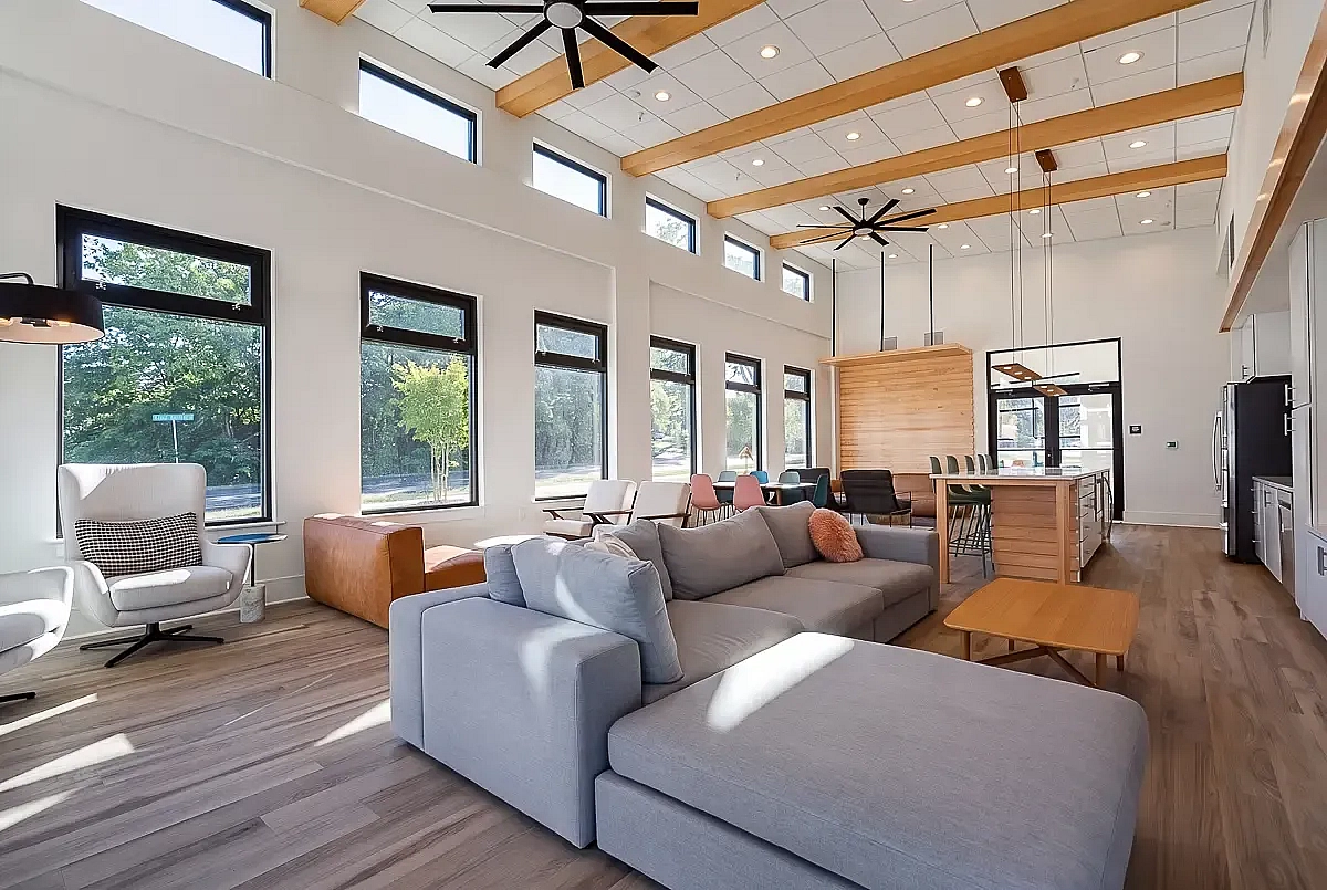 Bright and spacious modern resident clubroom at 5 Row Apartments with high ceilings, large windows, and stylish wooden beams, featuring plush seating and a contemporary open kitchen.