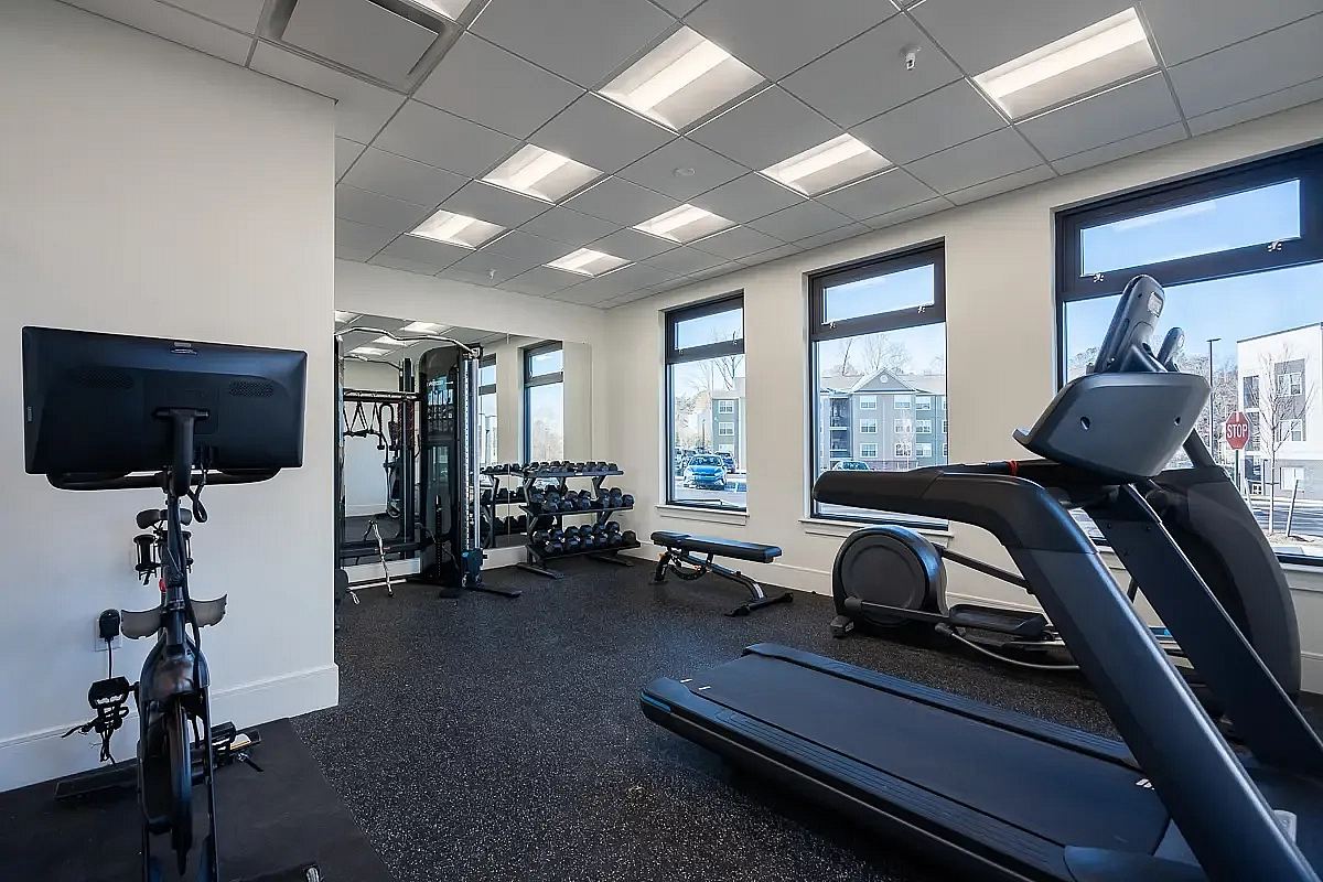 Modern apartment gym featuring a treadmill, cycling machine, and weights with large windows allowing ample natural light at 5 Row Apartments.