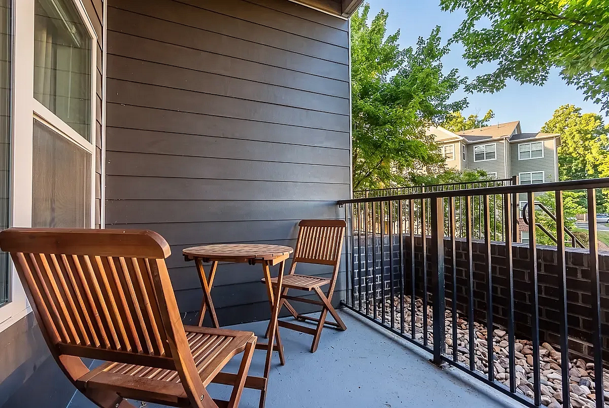 Charming balcony with cozy wooden furniture offering a serene outdoor space with lush greenery views at 5 Row Apartments in Charlottesville, Virginia.