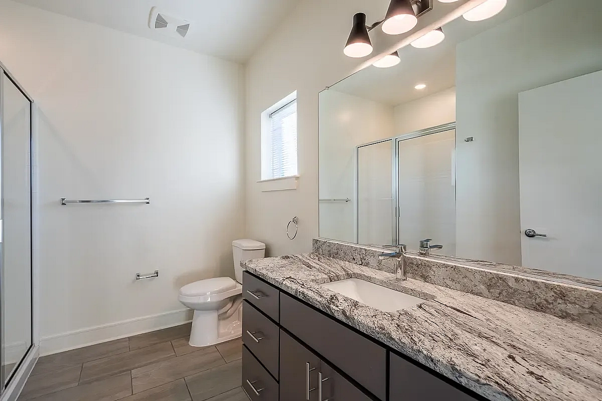 Elegant bathroom featuring modern lighting, a large granite countertop with sleek fixtures, and a spacious shower.