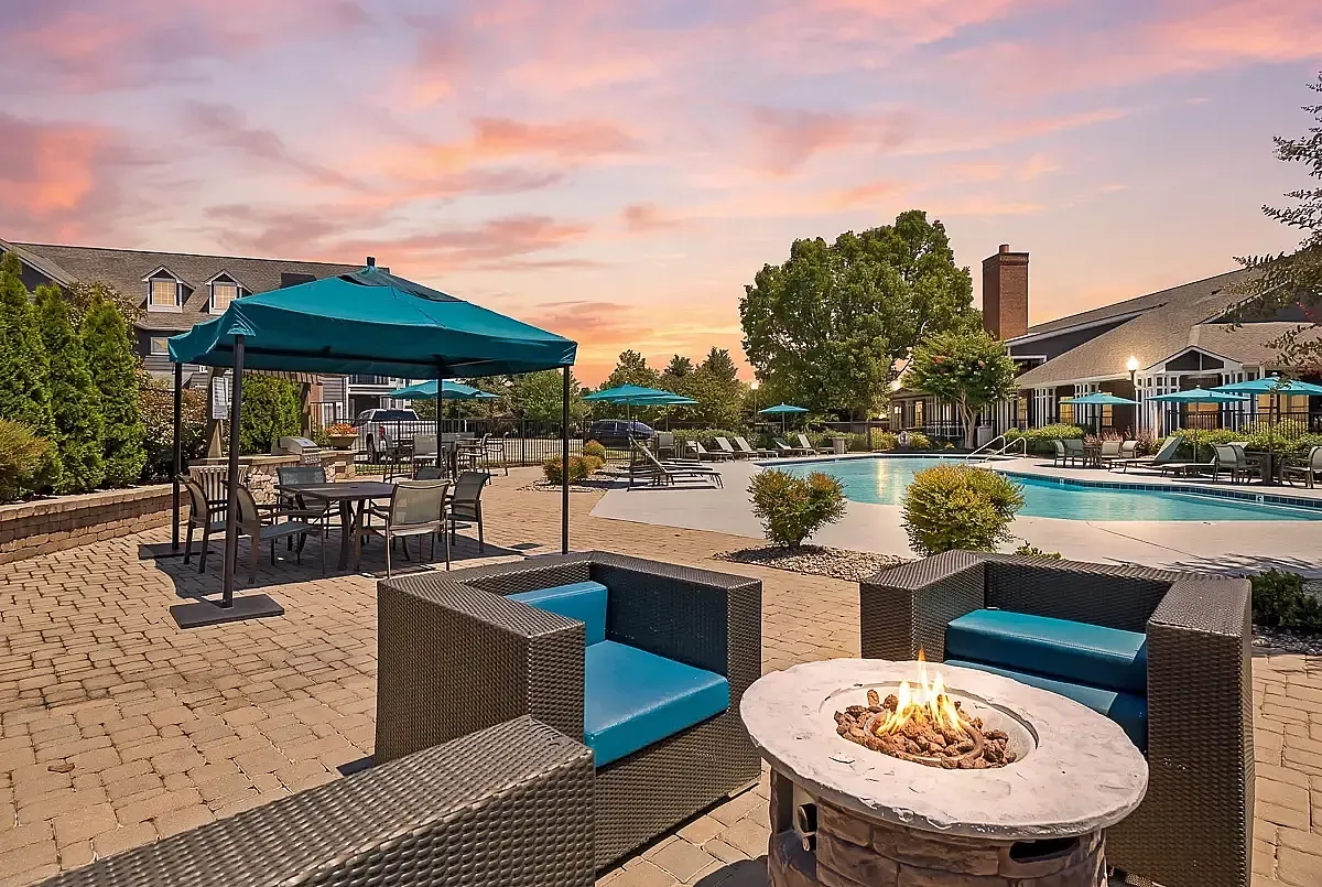 Luxurious outdoor pool area at Cason Estates Apartments with cozy fire pit, stylish lounge chairs, and vibrant umbrellas against a stunning sunset.