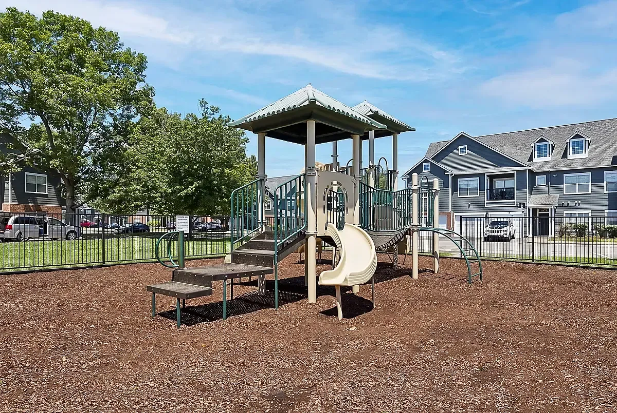 Inviting playground at Cason Estates in Murfreesboro, TN with vibrant slide and climbing structure surrounded by lush greenery and secure fencing, perfect for family fun.