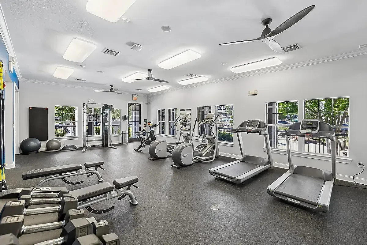 Modern fitness center with state-of-the-art equipment, including treadmills, weight benches, and a variety of exercise machines, surrounded by bright windows.