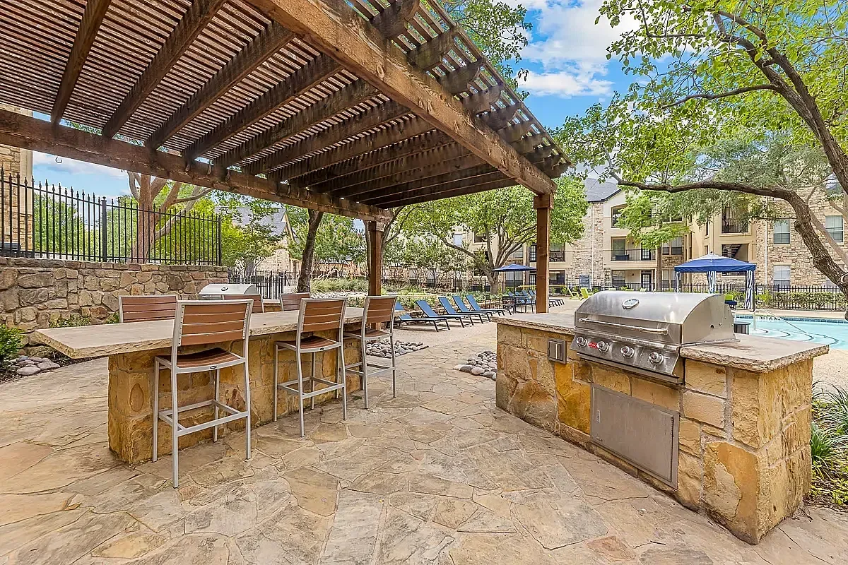 Charming outdoor patio with pergola, featuring a built-in grill and bar seating, adjacent to a refreshing pool area.