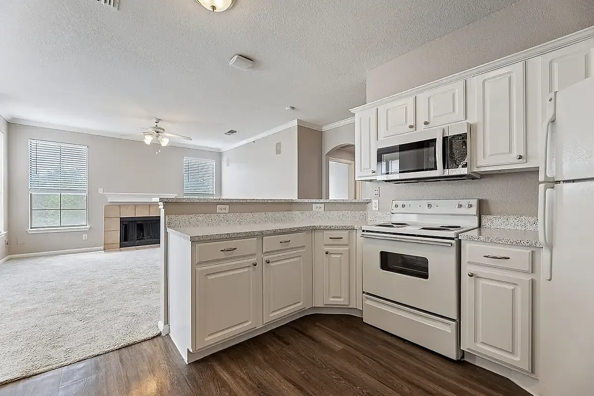 Bright and spacious kitchen with modern white cabinetry, granite countertops, and airy connected living room featuring large windows and cozy fireplace.