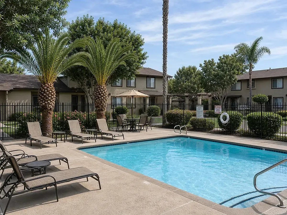 Inviting outdoor pool area surrounded by lush greenery and lounge chairs, perfect for relaxation and leisure Camelot Apartments in Yuma, AZ.