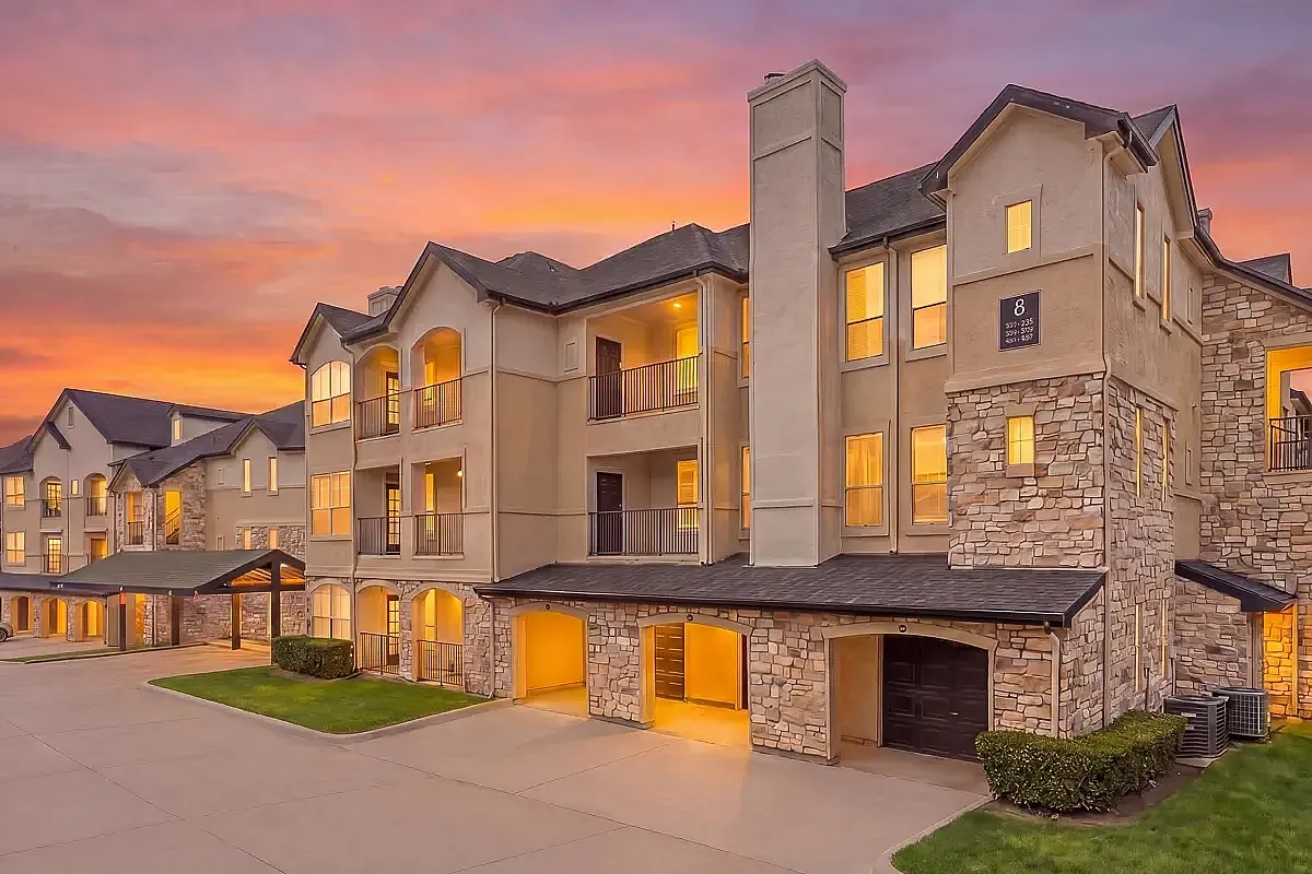 Charming apartment complex with stone accents illuminated at sunset, showcasing elegant architecture and warm, inviting atmosphere at Stonebriar of Frisco Apartments in Frisco, Texas.