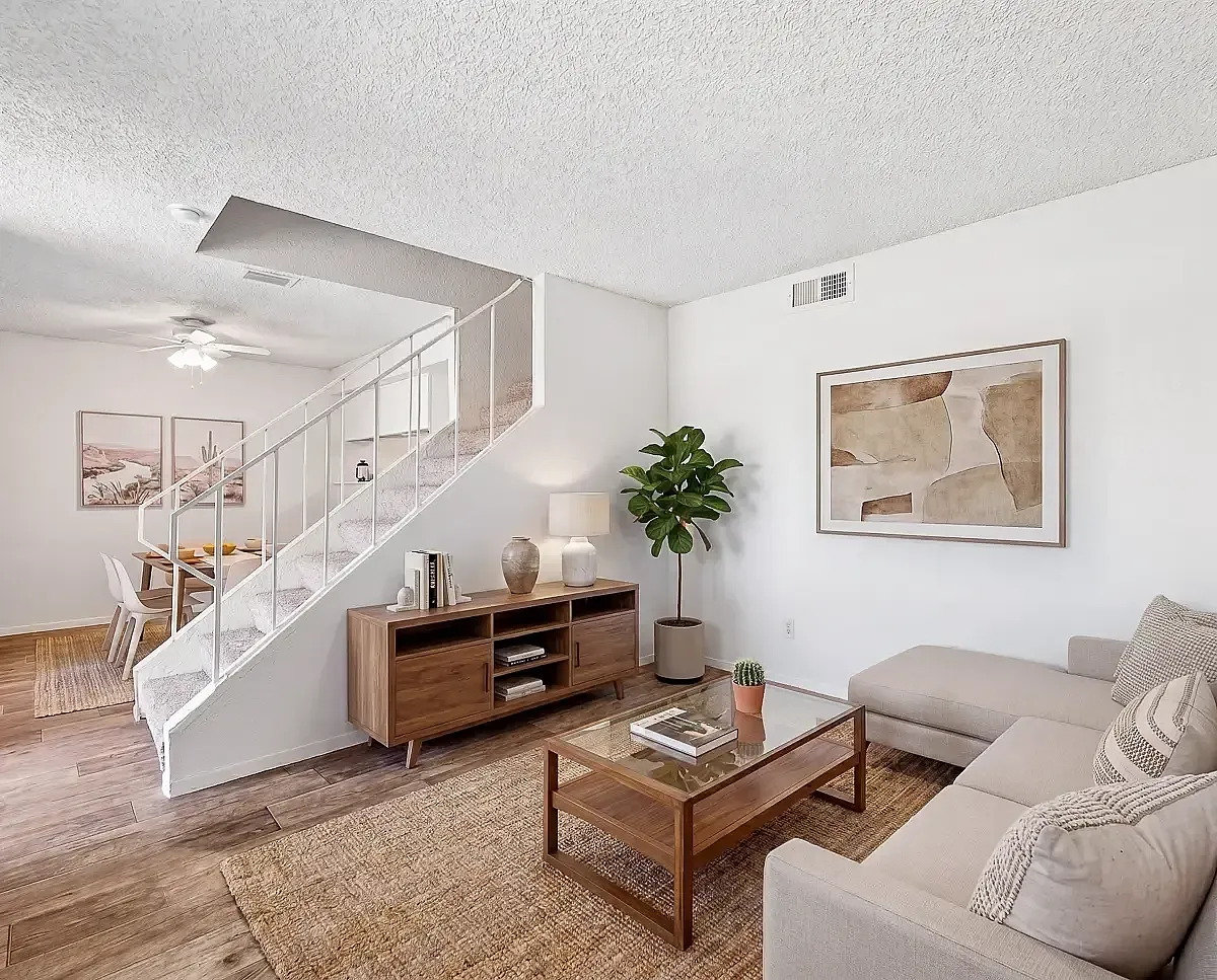 Stylish modern living room with light wood flooring, cozy beige sofas, and elegant wooden furniture, complemented by vibrant green plants and a sleek wall-mounted TV.