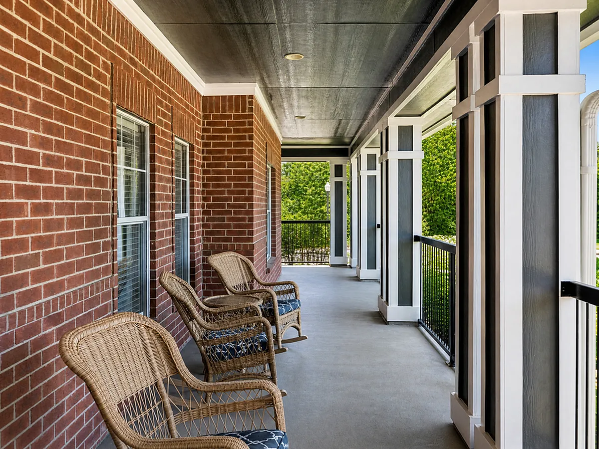 Inviting balcony with elegant wicker chairs, brick walls, and lush greenery views, perfect for relaxation.