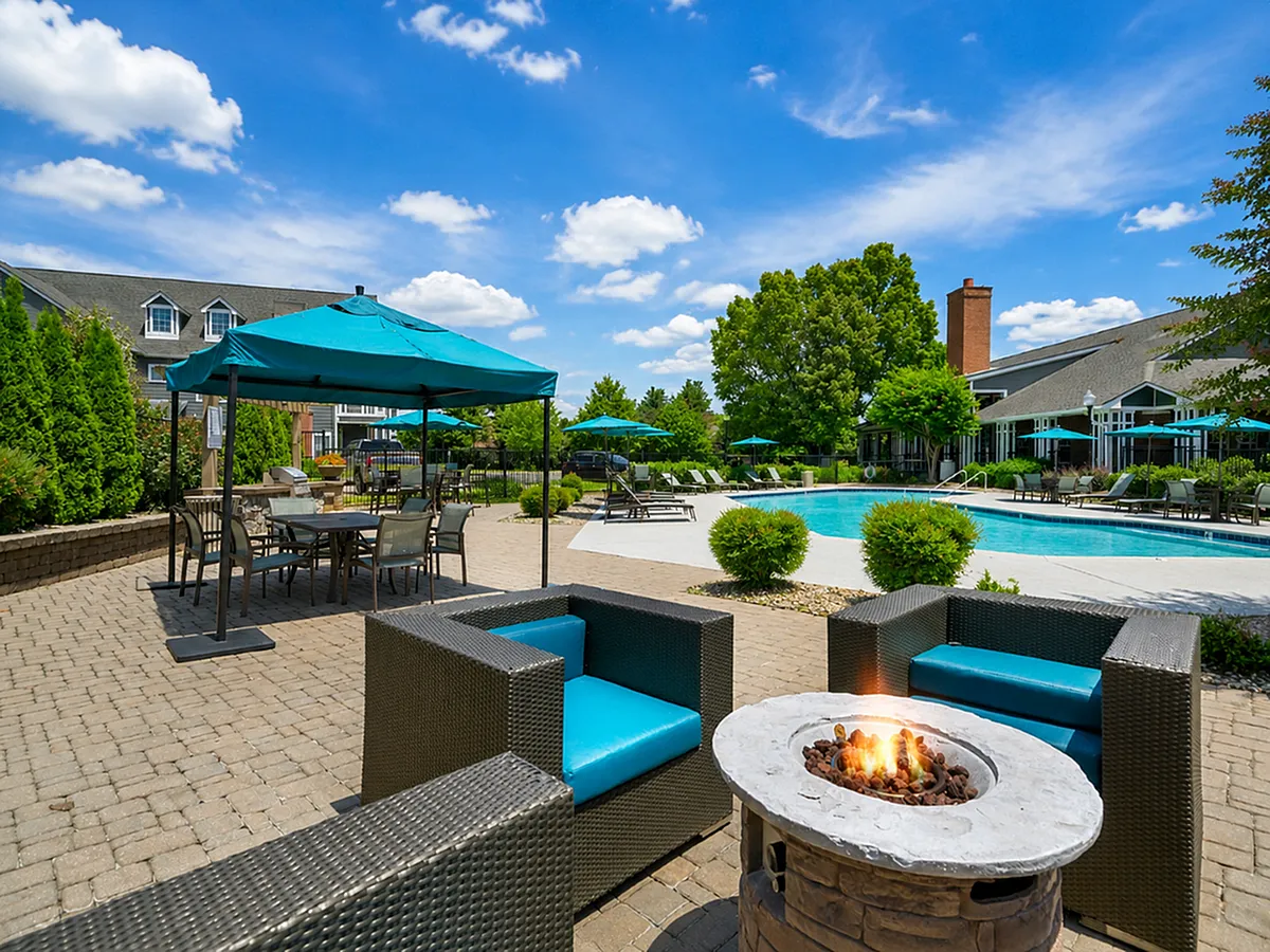 Luxurious apartment complex courtyard with inviting pool, cozy fire pit seating, and elegant outdoor dining under vibrant blue umbrellas.