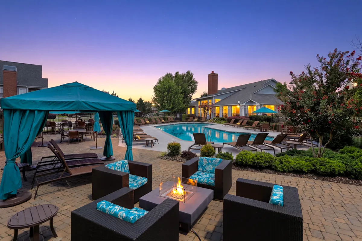 Luxurious outdoor space featuring a sparkling pool, stylish seating under teal gazebos, and lush landscaping at sunset.