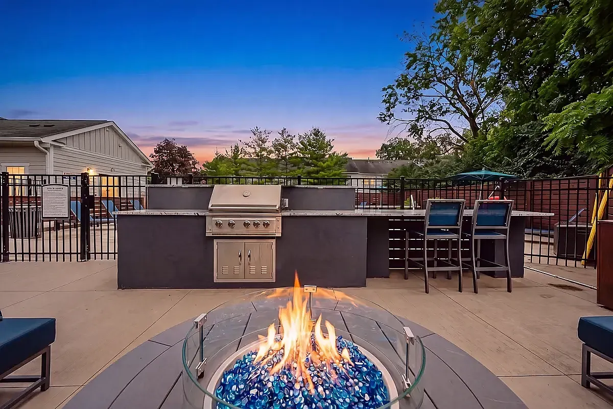 Charming outdoor patio space featuring a modern grill station and cozy fire pit under a vibrant sunset sky at Alkire Glen Apartments.