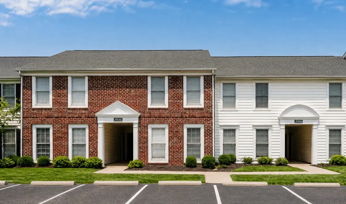 Charming duplex with classic red brick and white siding facade, featuring inviting entryways and well-maintained landscaping, set against a bright blue sky.